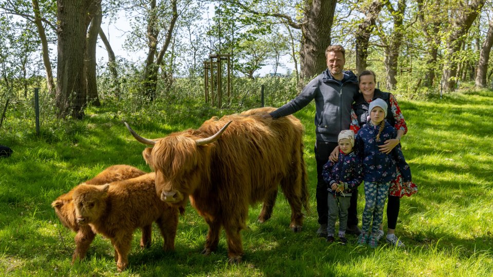 Matthias und Nicolle Schilling stehen mit Ihren beiden Töchtern neben einem braunen Highland-Rind im Grünen auf der Insel Öhe