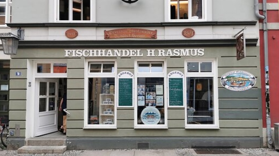 Die Ausßenfassade des traditionellen Fischhandesl Rasmus in Stralsund mit vielen Schildern und Tafeln.