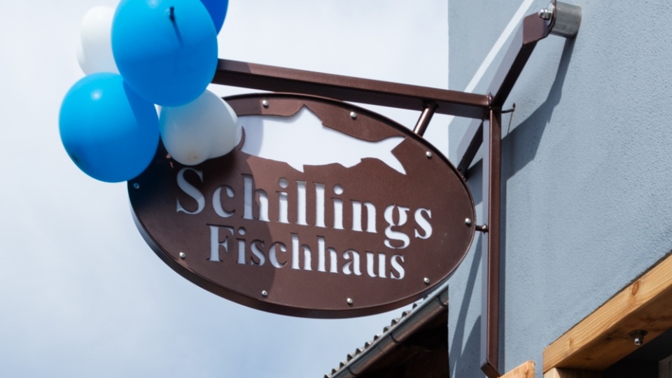 Zu sehen ist das Eingangsschild von Schillings Fischhaus in Schaprode, ein Schild mit einem ausgeschnittenen Fisch in braunem Metall.