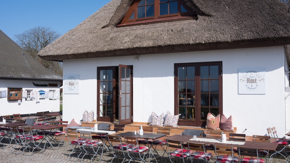Das Restaurant Hafenamt in Kloster auf Hiddensee ist ein weißen restgedecktes Haus mit einladenden Sitzgelegenheiten direkt vor dem Haus.