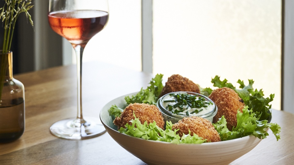 Zu sehen sind lecker angerichtete Hechtbällchen auf Salat und nebendran steht ein Glas Rosé. Die Hechtbällchen gibt es im Restaurant Das Rote Haus auf Vitte in Hiddensee.